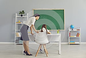 Teacher standing and checking girl pupil sitting and doing homework in school