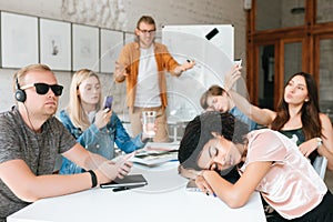 Teacher standing near board and amazedly looking at students. Group of young students making photos, listening music and