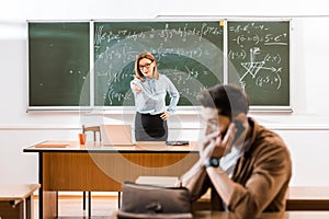 Teacher standing near chalkboard and speaking with student who talking