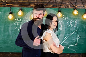 Teacher and strict schoolmaster look confident. Lady and hipster working together in school. Man with beard and