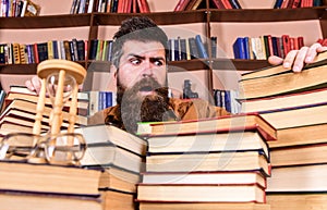 Teacher or student with beard sits at table with books, defocused. Bibliophile concept. Man on confused face between