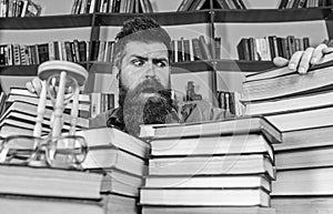 Teacher or student with beard sits at table with books, defocused. Bibliophile concept. Man on confused face between