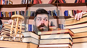 Teacher or student with beard sits at table with books, defocused. Man on frightened face between piles of books, while