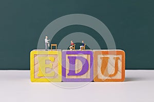 Teacher and student figurines standing on EDU wooden letter blocks