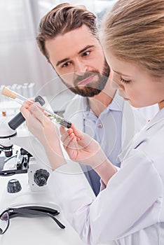 Teacher and student scientists examining green plant with soil in test tube