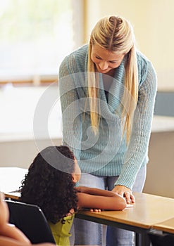 Teacher, student and talking at desk for education, learning and knowledge in a classroom. Professional woman helping