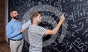 Teacher and student writing on big blackboard with mathematical
