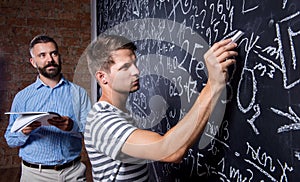 Teacher and student writing on big blackboard with mathematical