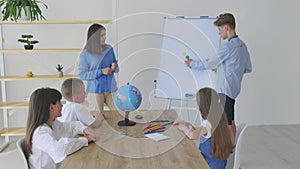 A teacher and students of different ages at a geography lesson. The student answers by standing near the board and tells the story