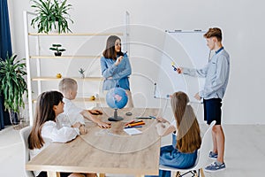 A teacher and students of different ages at a geography lesson. The student answers by standing near the board and tells the story