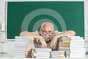 Teacher with too many books to read before exam. Teacher with books in school. Man school teacher standing in classroom