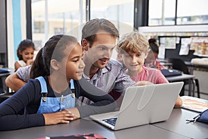 Teacher and two young students use laptop computer in class