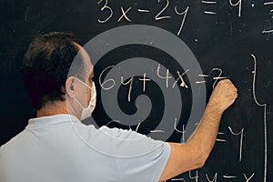 Teacher wearing mask writing equations on a blackboard. Covid situation, pandemic, new normal