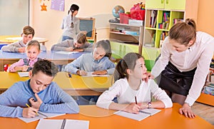 Teacher woman helping children during lesson in schoolroom photo