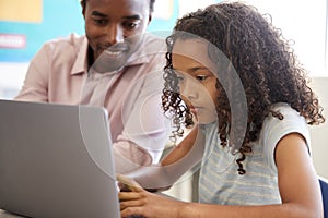 Teacher working with elementary school girl at laptop