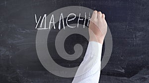 The teacher writes the text `Remote Learning` in Russian with chalk on the blackboard.