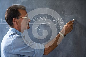 Teacher Writing Math Formulas On Blackboard At High School