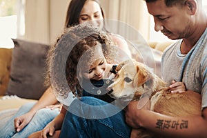 Teaching her responsibility while owning a pet. a young family sitting on the sofa at home and bonding with their dog.