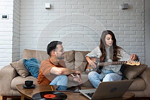 Teaching her to play guitar. Handsome young bearded man teaching his girlfriend to play guitar, sitting at home together. Musician