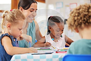 Teaching and kids looking happy while doing activity at kindergarten or pre-school. Smiling teacher sitting at table