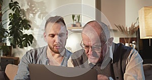 Teaching older people to use technology. Happy 30s caring young adult man helps senior dad with laptop, internet at home