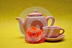 A teacup and a kettle with an orange rose