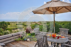 Teak dining table on a wooden deck overlooking the dunes and a walkway to the beach