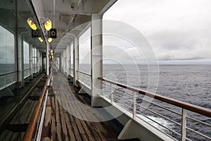 Teak lined Promenade Deck of modern cruise ship on a grey stormy