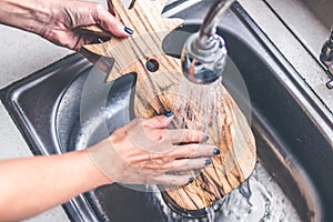 Teak wooden cutting board washing. Woman hands washing teak cutting board.