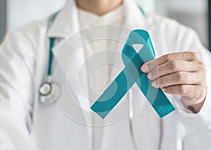 Teal awareness ribbon in doctor`s hand, symbolic bow color for supporting patient with Ovarian Cancer, PCOS and PTSD Illness