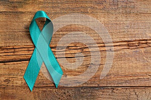 Teal awareness ribbon on wooden background, top view with space for text. Symbol of social and medical