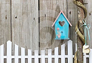 Teal blue birdhouse hanging over white picket fence