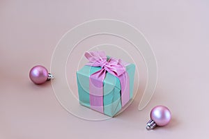 Teal blue gift box with pink bow and Christmas balls on beige background