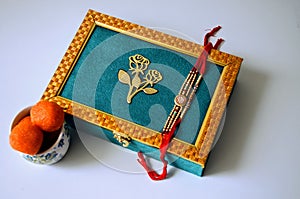 Teal and golden coloured dry fruit box with rakhis and ladoos white background. Hindu festival