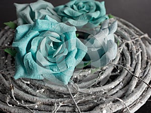 Teal paper flowers up close in a macro shot sitting on a coiled up wooden wreath with a black slate background.