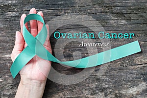 Teal ribbon on helping hand support for raising awareness on Ovarian Cancer illness in women`s health