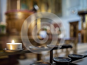Tealight candle burning in front of a church interior altar area