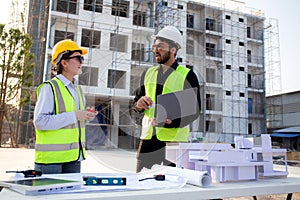 Team architect and builder talking and holding laptop looking model house at construction site.
