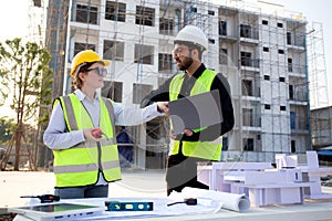 Team architect and builder talking and holding laptop looking model house at construction site.