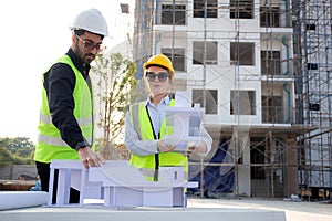 Team architect and builder talking and holding model house at construction site.