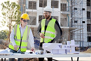 Team architect and builder talking and holding model house at construction site.