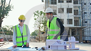 Team architect and builder talking and holding model house at construction site.