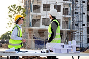 Team architect and builder talking and holding model house at construction site.