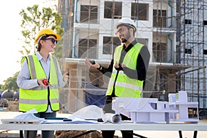 Team architect and builder talking and holding model house at construction site.