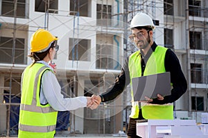 Team architect or engineer holding laptop looking model house and doing agreement while handshake together.