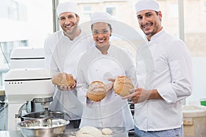 Team of bakers smiling at camera holding bread