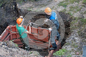 A team of builders is engaged in the repair of a sewer well. Reinforced concrete rings in the well. Trenchless re-laying or