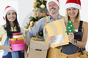 Team of builders are holding gift boxes and tools on background of New Year tree