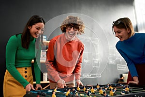 Team-building activities. Group young and excited people in casual wear playing table soccer in the modern office and