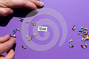Team building. Word TEAM with miniatures of people on a colored background. Concept to describe HR job activity and the building